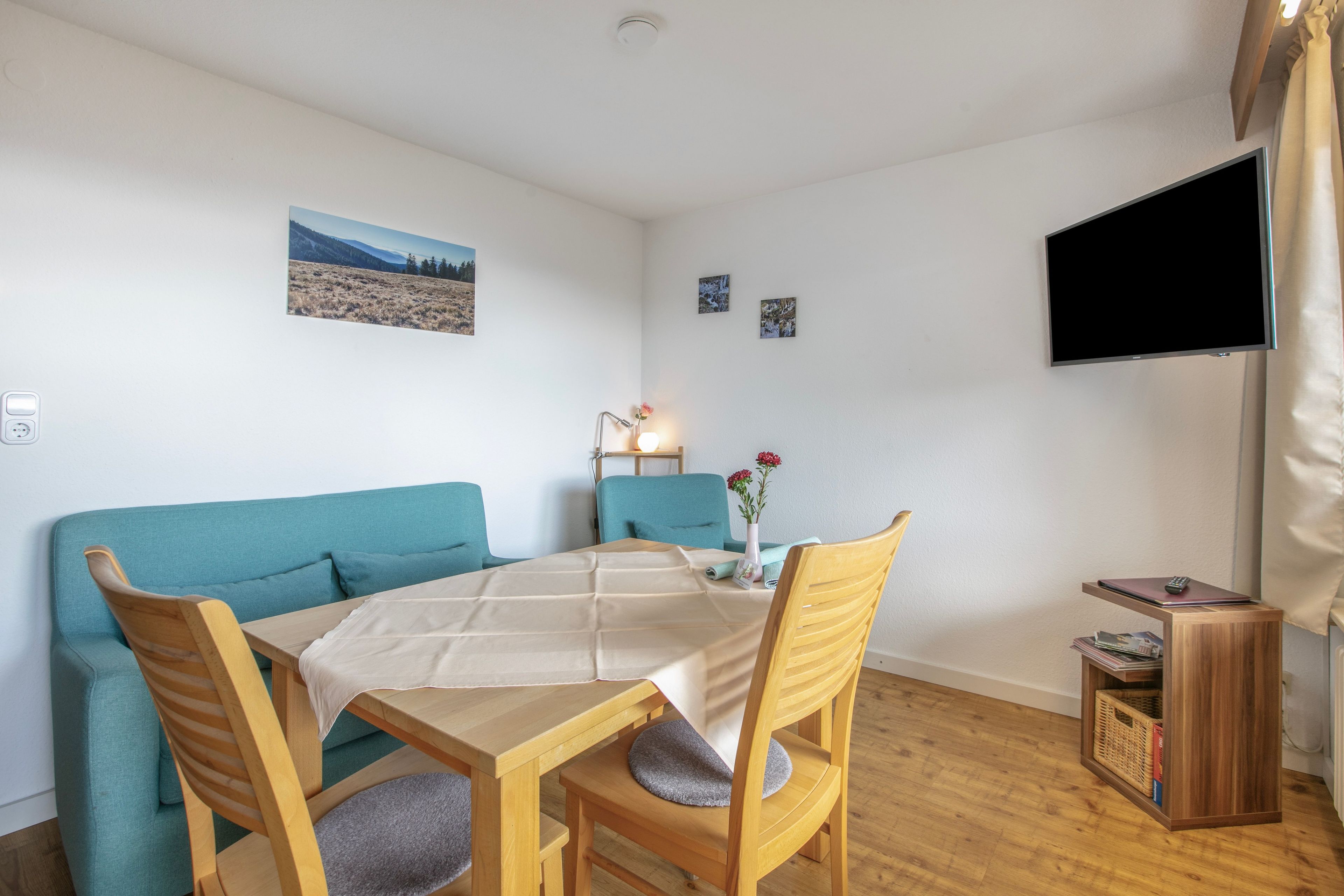 A cozy room with a sofa, a dining table, and chairs. There's a flat-screen TV mounted on the wall.