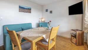 Ett mysigt rum med en soffa, ett matbord och stolar. En platt-TV är monterad på väggen.