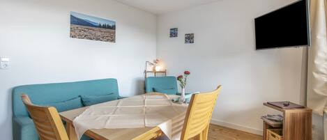 Een gezellige kamer met een bank, een eettafel en stoelen. Er is een flatscreen televisie aan de muur bevestigd.