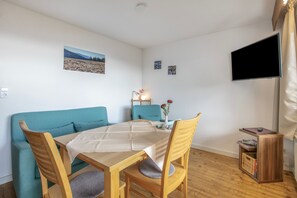 A cozy room with a sofa, a dining table, and chairs. There's a flat-screen TV mounted on the wall. - Wiesentalblick Apartment with Mountain View and Balcony (Todtnau)
