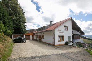 A two-story house with a sloped roof, a car parked in front, and a paved driveway. - Wiesentalblick Apartment with Mountain View and Balcony (Todtnau)