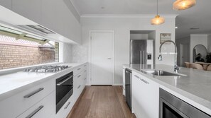 Une cuisine moderne équipée d’une cuisinière à gaz, d’appareils électroménagers en acier inoxydable, d’un lave-vaisselle et d’un grand îlot central doté d’un évier.