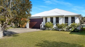 A modern two-story house with a garage, a front lawn, and mature trees. - Mibilla House in Sussex Inlet (Sussex Inlet)