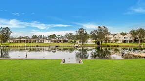 A lakeside view of a residential area with houses, a dock, and a grassy area. - Mibilla House in Sussex Inlet (Sussex Inlet)