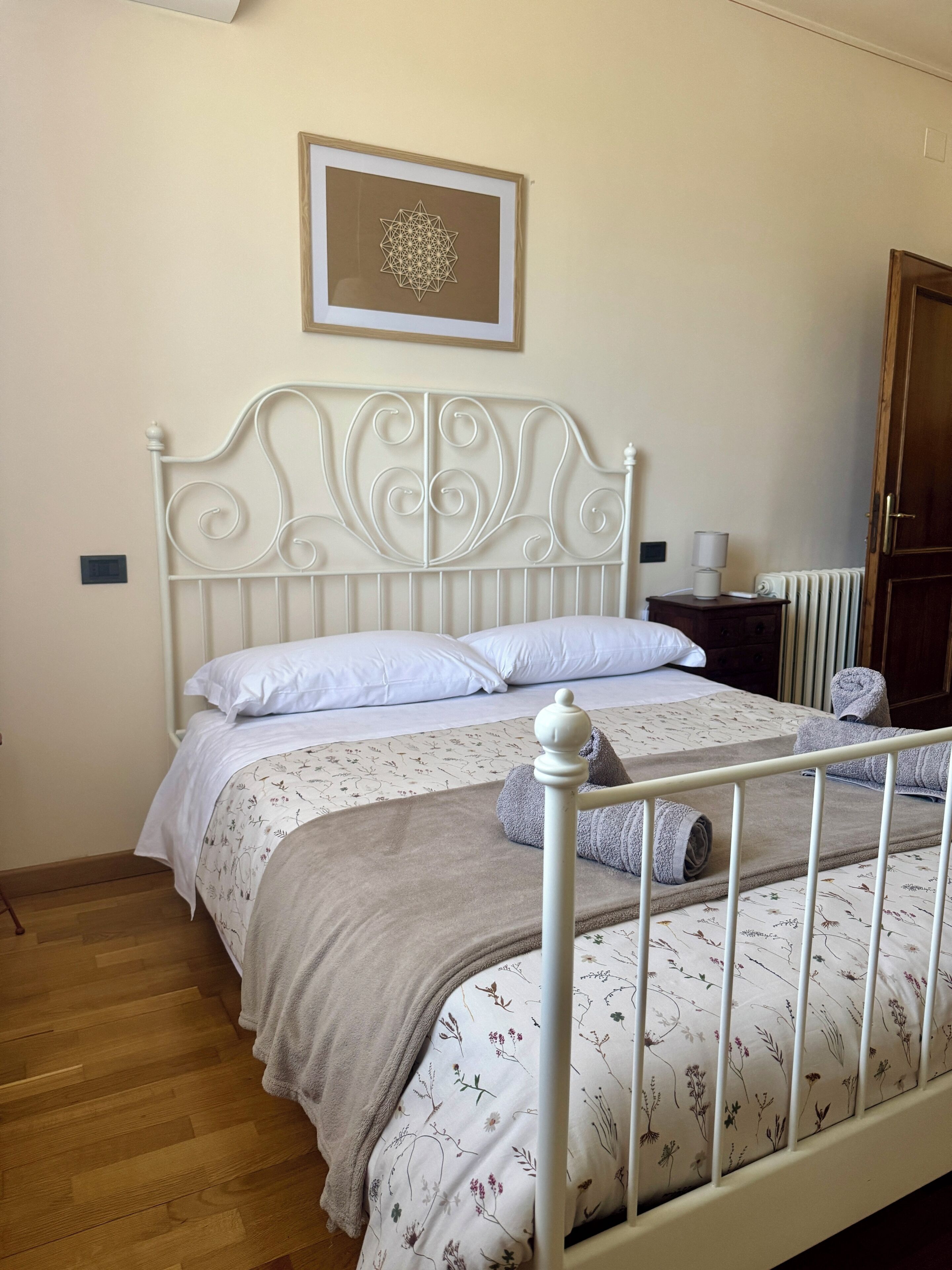A bed with a white metal frame, a floral-patterned bedspread, and a beige blanket.