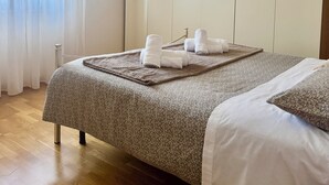 Une chambre d’hôtel avec un lit, une armoire, une fenêtre avec des rideaux et une lampe suspendue.