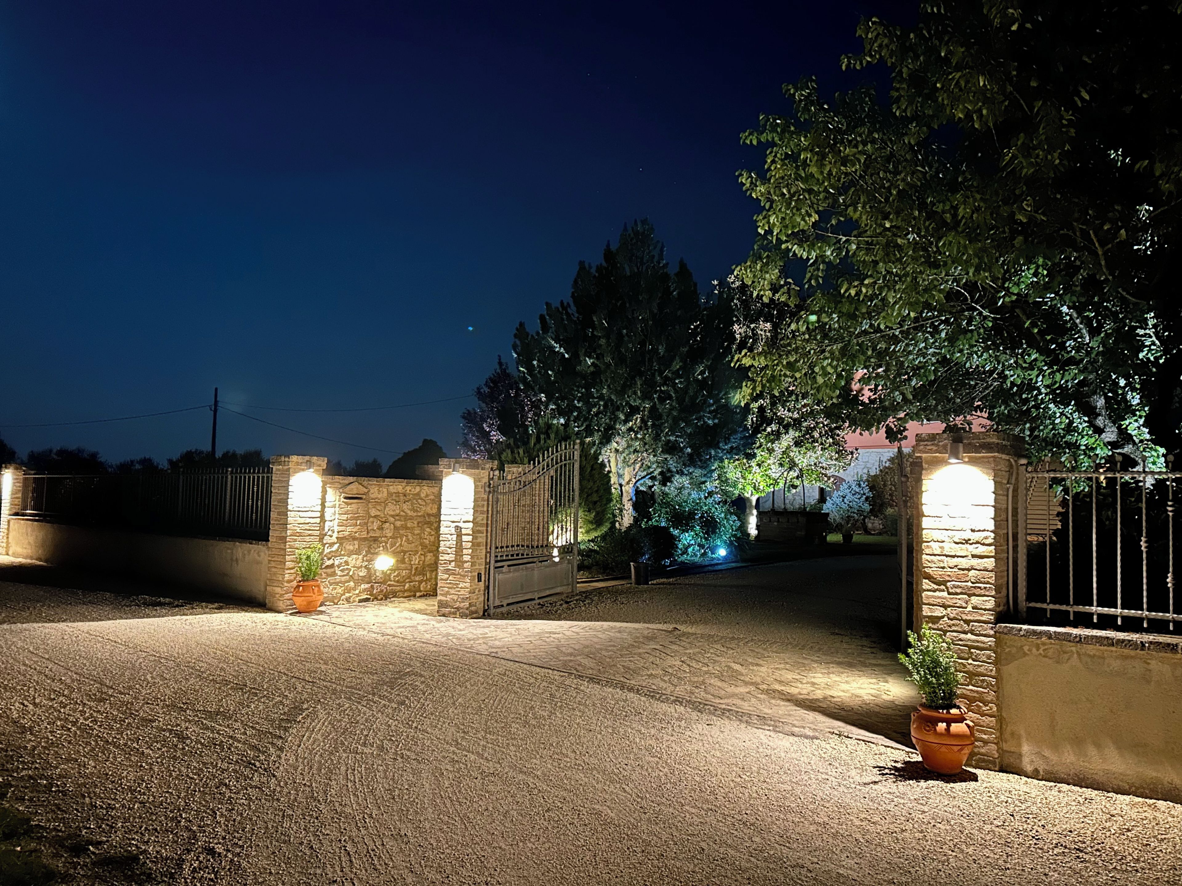 A gated driveway at night with stone walls and a potted plant.