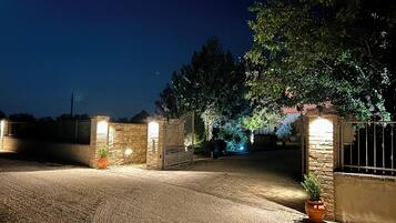 A gated driveway at night with stone walls and a potted plant.