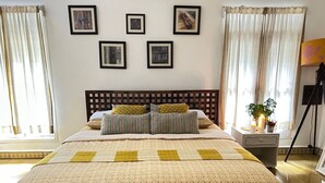 A bedroom with a bed, curtains, framed pictures, a nightstand, and a lamp.