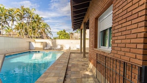 Ein Swimmingpool mit Fliesen, einer Ziegelwand und einer überdachten Terrasse.