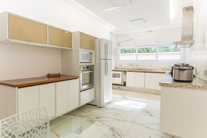 A modern kitchen with white cabinetry, a marble countertop, and a window providing natural light. - Casa com 3 Suítes, Piscina e Churrasqueira (Guarujá)