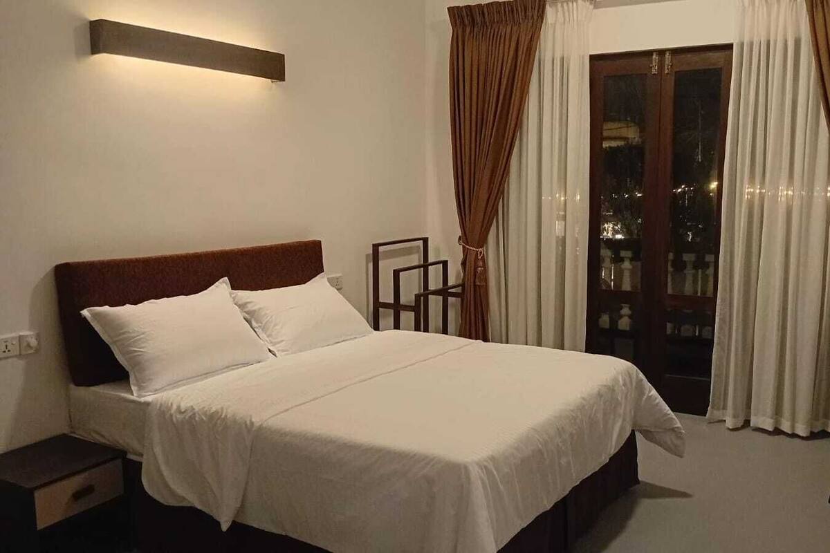 A bedroom with a bed, nightstands, a desk, and a window with curtains.