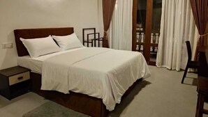 Un dormitorio con cama, mesitas de noche, una silla y vistas a un balcón con cortinas.