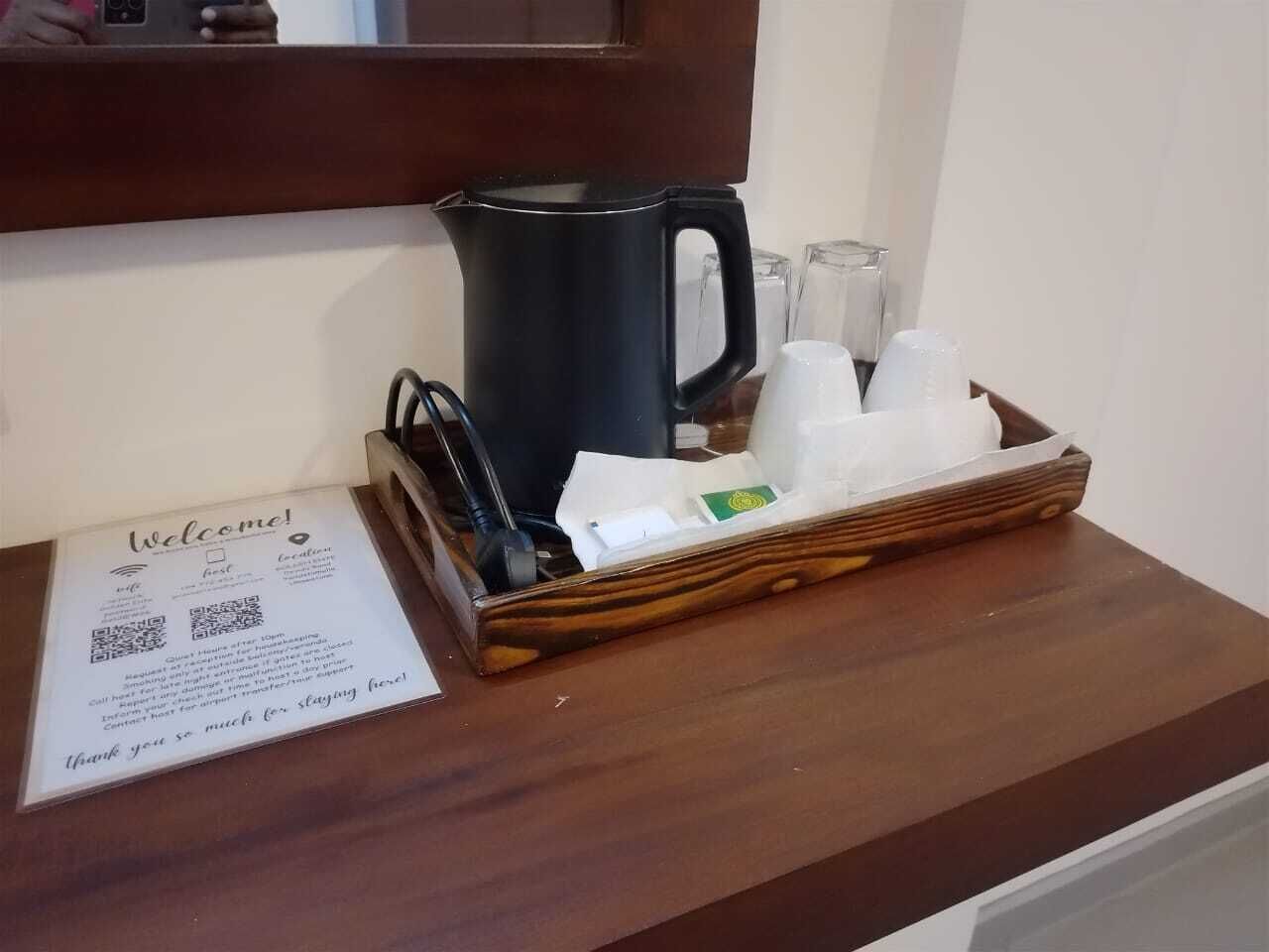 A welcome sign with a QR code, a black coffee pot, and a tray with cups and a tissue box on a wooden counter.