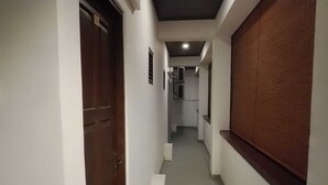 Un pasillo con puerta de madera, paredes blancas e iluminación empotrada en el techo.