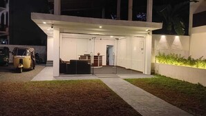 Un edificio moderno con un espacio exterior cubierto, un vehículo estacionado fuera y un césped cuidado.