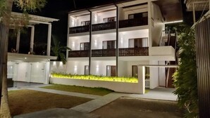 Un edificio de varios pisos con balcones, una entrada cubierta y un exterior bien iluminado.