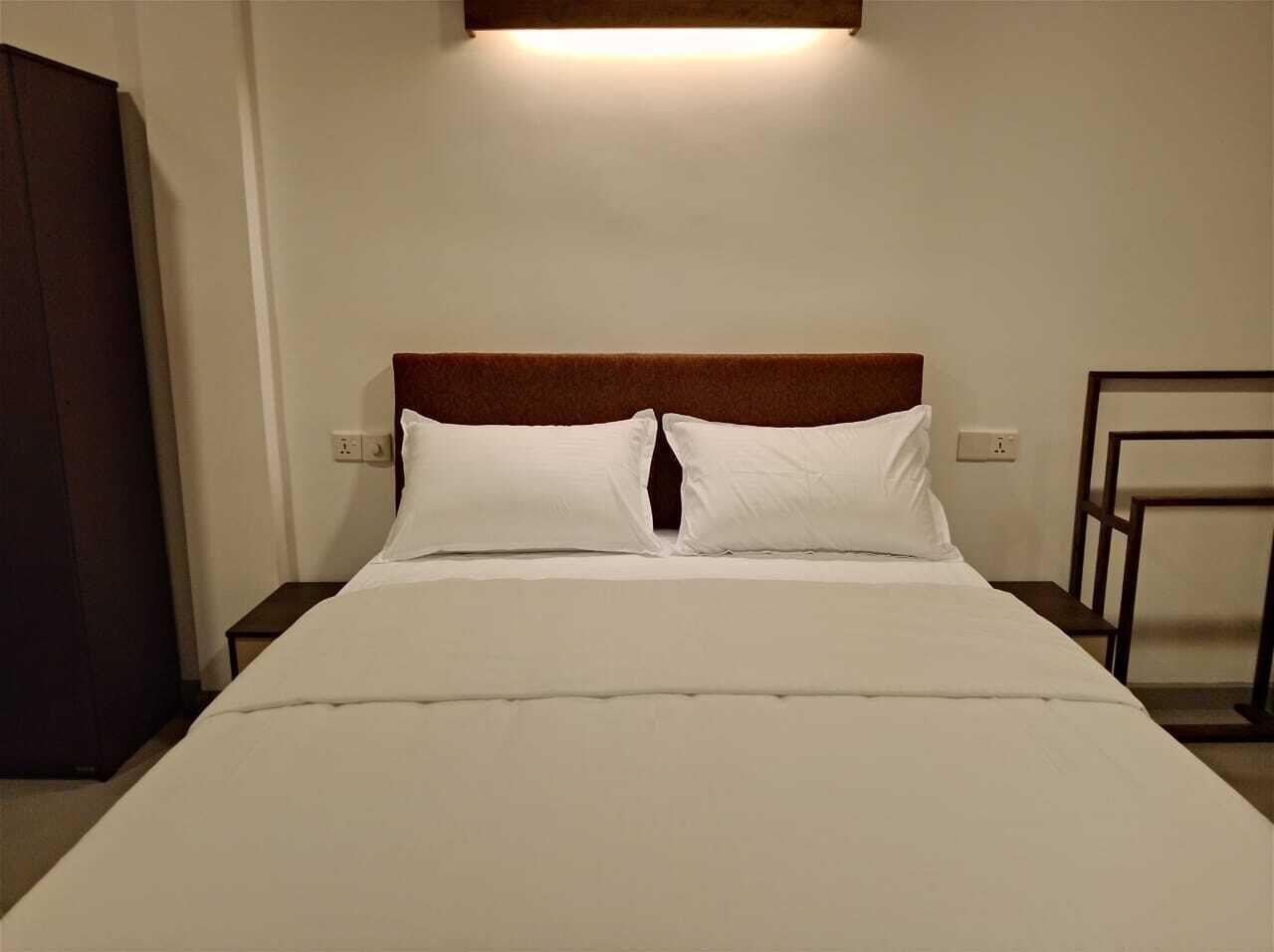 A neatly made bed with a wooden headboard, white bedding, and a bedside table with a lamp.