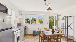 Une cuisine équipée d’un lave-linge, d’une table à manger avec des chaises et d’une fenêtre donnant sur un espace verdoyant.
