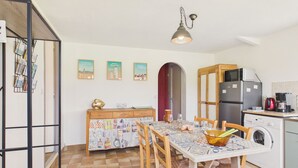 Une cuisine équipée d’une table à manger, de chaises, d’un réfrigérateur, d’un lave-linge et d’un luminaire suspendu.