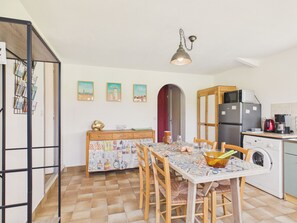 A kitchen with a dining table, chairs, a refrigerator, a washing machine, and a hanging light fixture. - House for 4 with garden and terrace in a quiet area (Sarzeau)