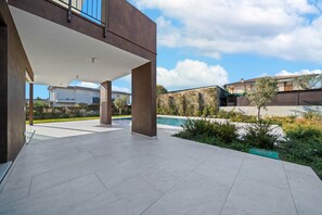 Eine moderne Außenpatio-Terrasse mit einem Schwimmbad, umgeben von viel Grün und einer Steinmauer.