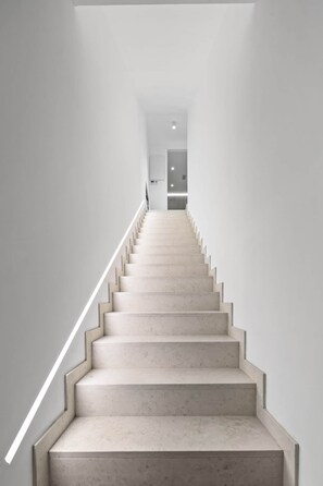 Eine moderne, minimalistisch gestaltete Treppe, die zu einem Raum mit einer Tür und einer Lampe führt.