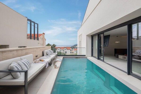 A modern outdoor pool area with a sofa and a dining table, a clear view of the cityscape, and a large window.