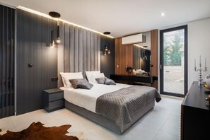 A modern bedroom with a large bed, bedside tables, a mirror, and a view through a glass door.