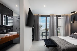 A modern bedroom with a large bed, a built-in TV, a bathroom with a mirror, and a balcony with a view.