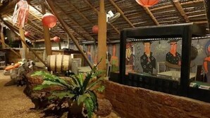 Un restaurante con una decoración rústica, que presenta un tejado de paja, barriles de madera y un mural en la pared.