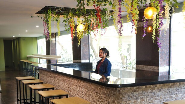 A bar area with a counter, stools, hanging plants, and a person behind the counter. - C Suites Gilbert (Bengaluru)