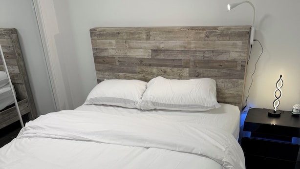 Una cama con ropa de cama blanca, un cabecero de madera y una mesita de noche con una lámpara.