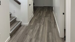 Un pasillo con piso de madera, paredes blancas y una puerta al final.