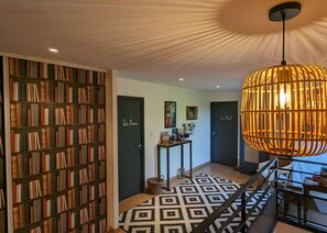 A hallway with a bookshelf, a patterned rug, a staircase, and a hanging light fixture. - Guest Room 'L'Abri des Flots' with Shared Pool, Terrace, and Wi-Fi (Plouër-sur-Rance)
