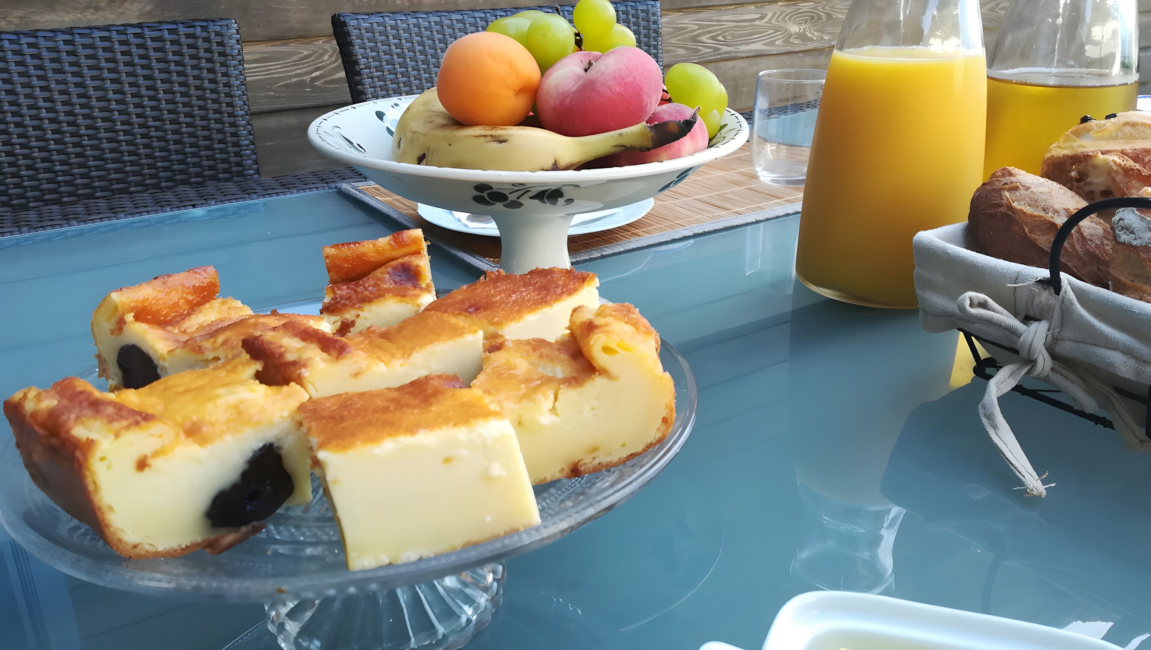 A table with a fruit bowl, a glass of orange juice, and a plate of custard pies.
