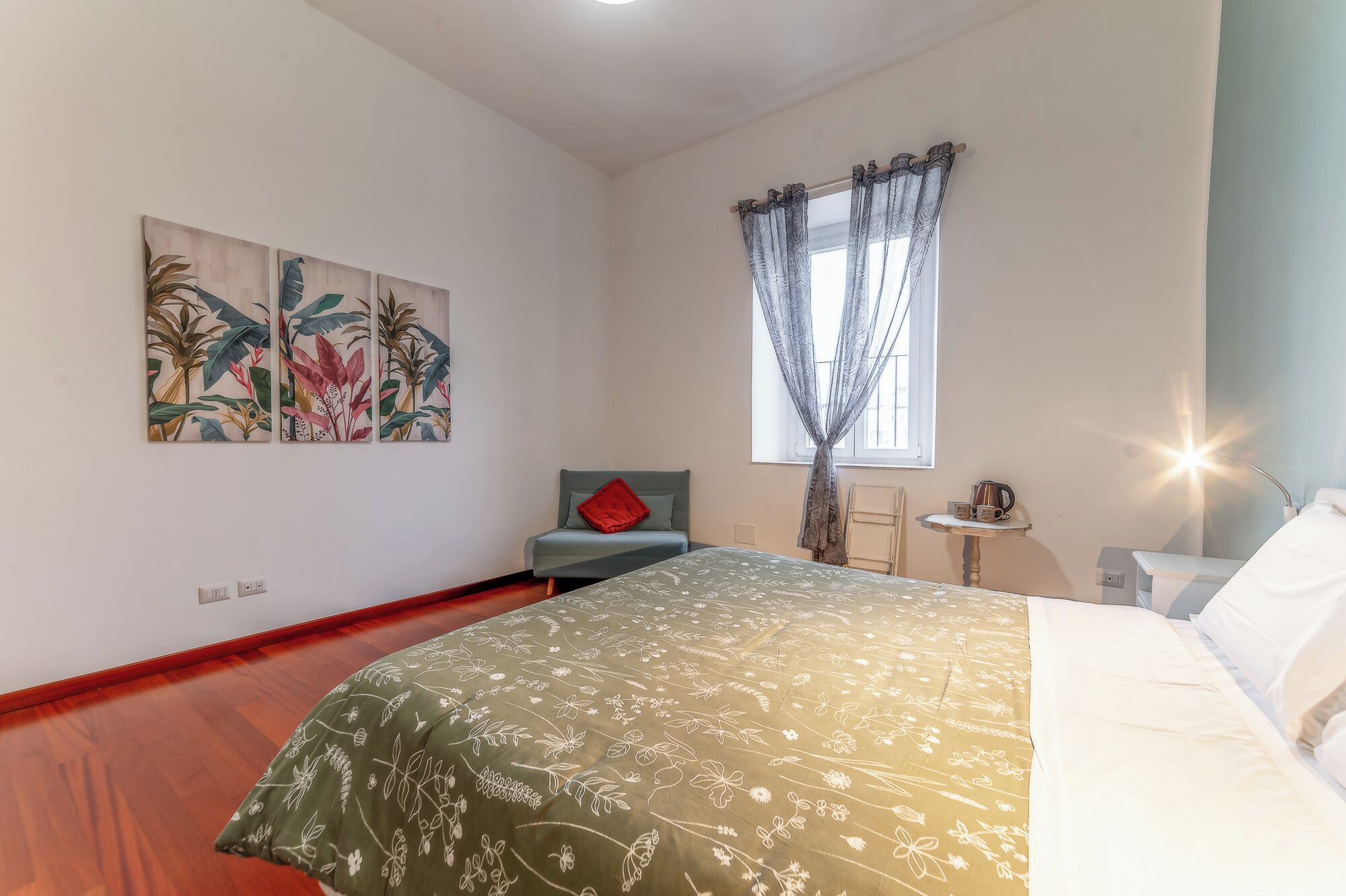 A bedroom with a bed, a chair, a small table, and two wall-mounted paintings.
