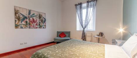 A bedroom with a bed, a chair, a small table, and two wall-mounted paintings.