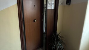 Un couloir avec une porte en bois, une plante en pot, une poubelle et un panneau sur le mur.