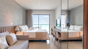 Une chambre d’hôtel moderne équipée de deux lits, d’un canapé, d’un bureau et d’une grande fenêtre donnant sur la mer.
