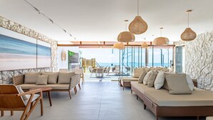 Un salon spacieux doté d’une grande fenêtre donnant sur la mer, de meubles en osier et de luminaires suspendus en fibres tressées.