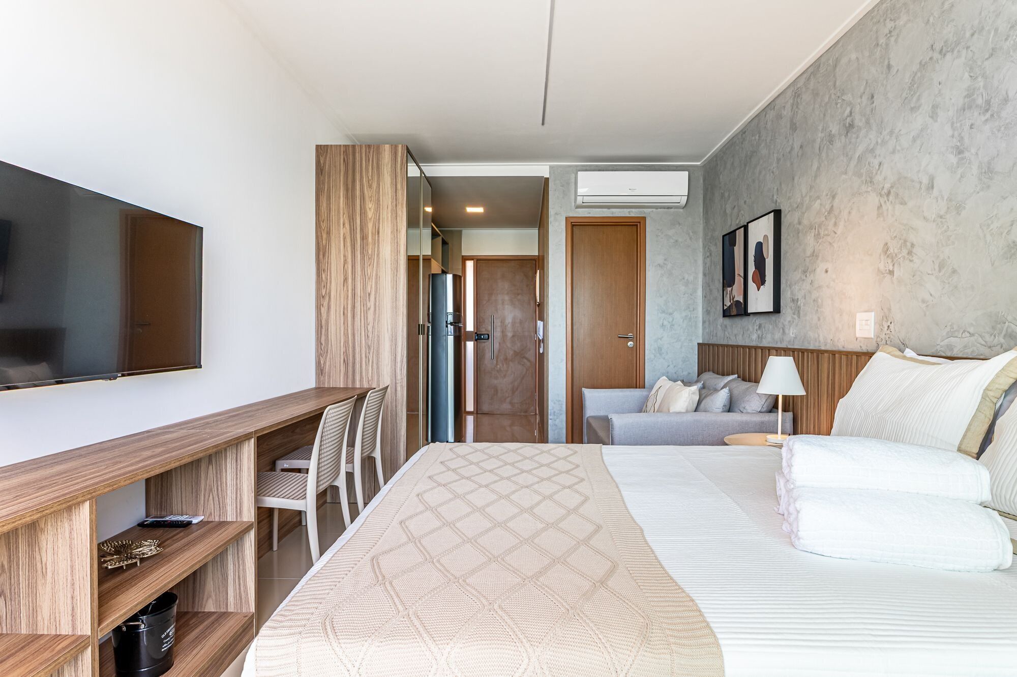 Ett hotellrum med en säng, ett skrivbord med stolar, en tv, en soffa och en luftkonditioneringsanläggning.