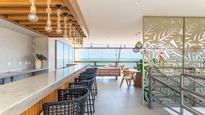 Un espace bar moderne avec vue sur l’océan, un plafond en bois et un élément décoratif servant de séparation.