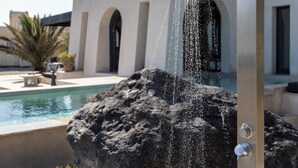 A modern outdoor water feature with a stone base, a metal structure, and a pool in the background. - Exomitis1 Cellar & Sea Escape (Santorini)