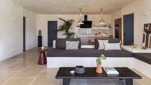 A modern living room with a sofa, a coffee table, and a kitchen in the background. - Exomitis1 Cellar & Sea Escape (Santorini)