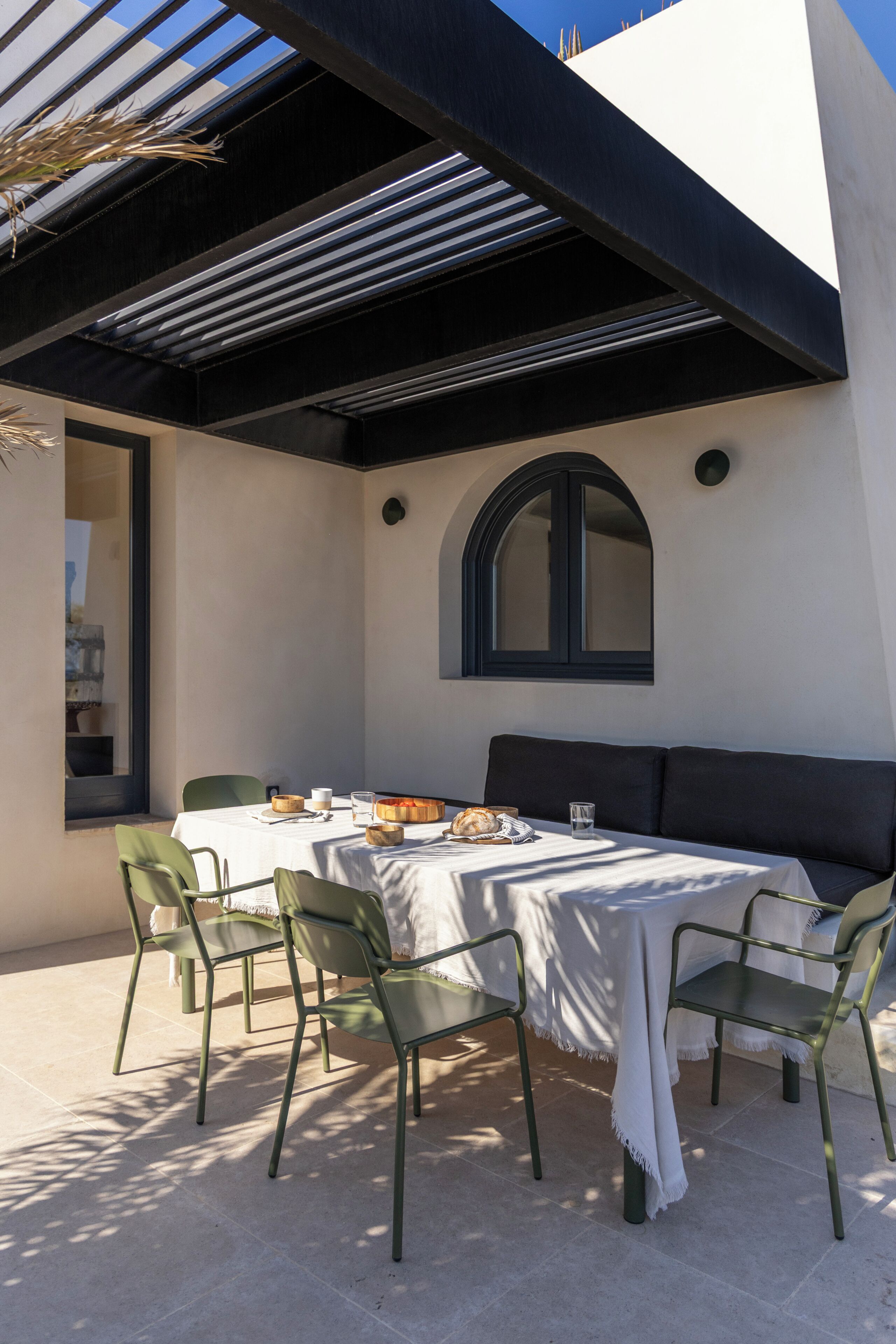 Ein Essbereich mit einem Tisch für vier Personen, umgeben von Stühlen, unter einer Pergola.