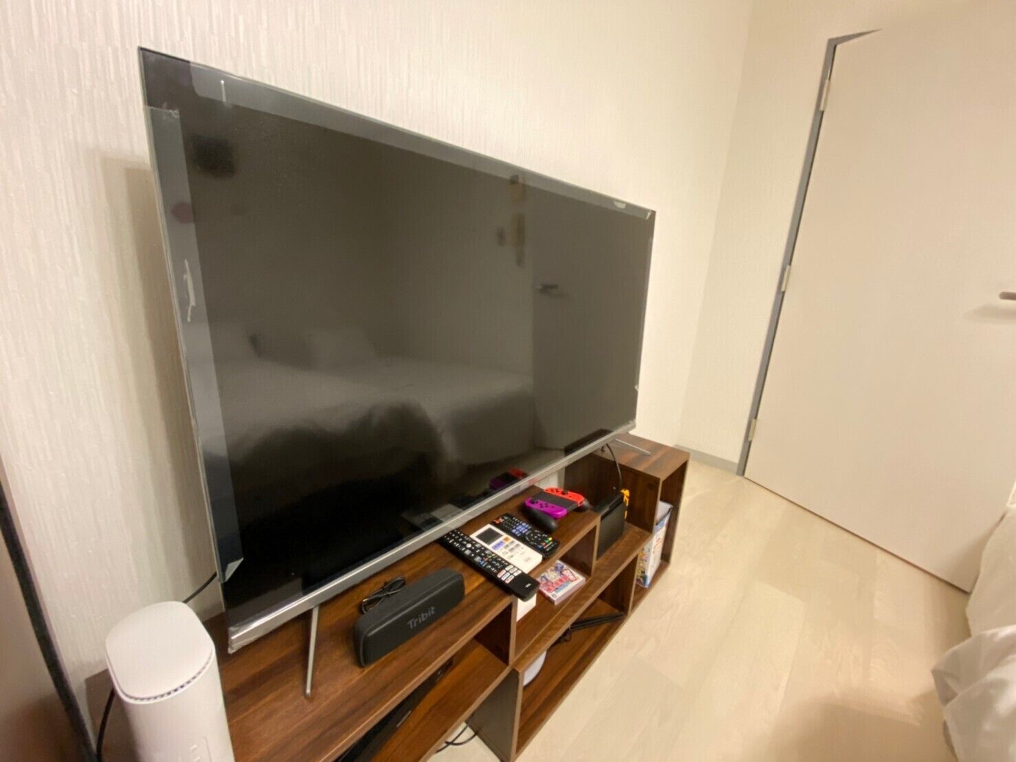 Een flatscreen televisie op een houten standaard, een afstandsbediening, een kleine speaker en een wit apparaat op de vloer.