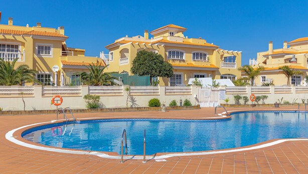 Una piscina con borde de baldosas, rodeada de edificios amarillos con balcones y ventanas.