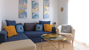Una sala de estar con un sofá, una mesa de centro y un sillón. Hay dos cuadros colgados en la pared y un adorno decorativo.