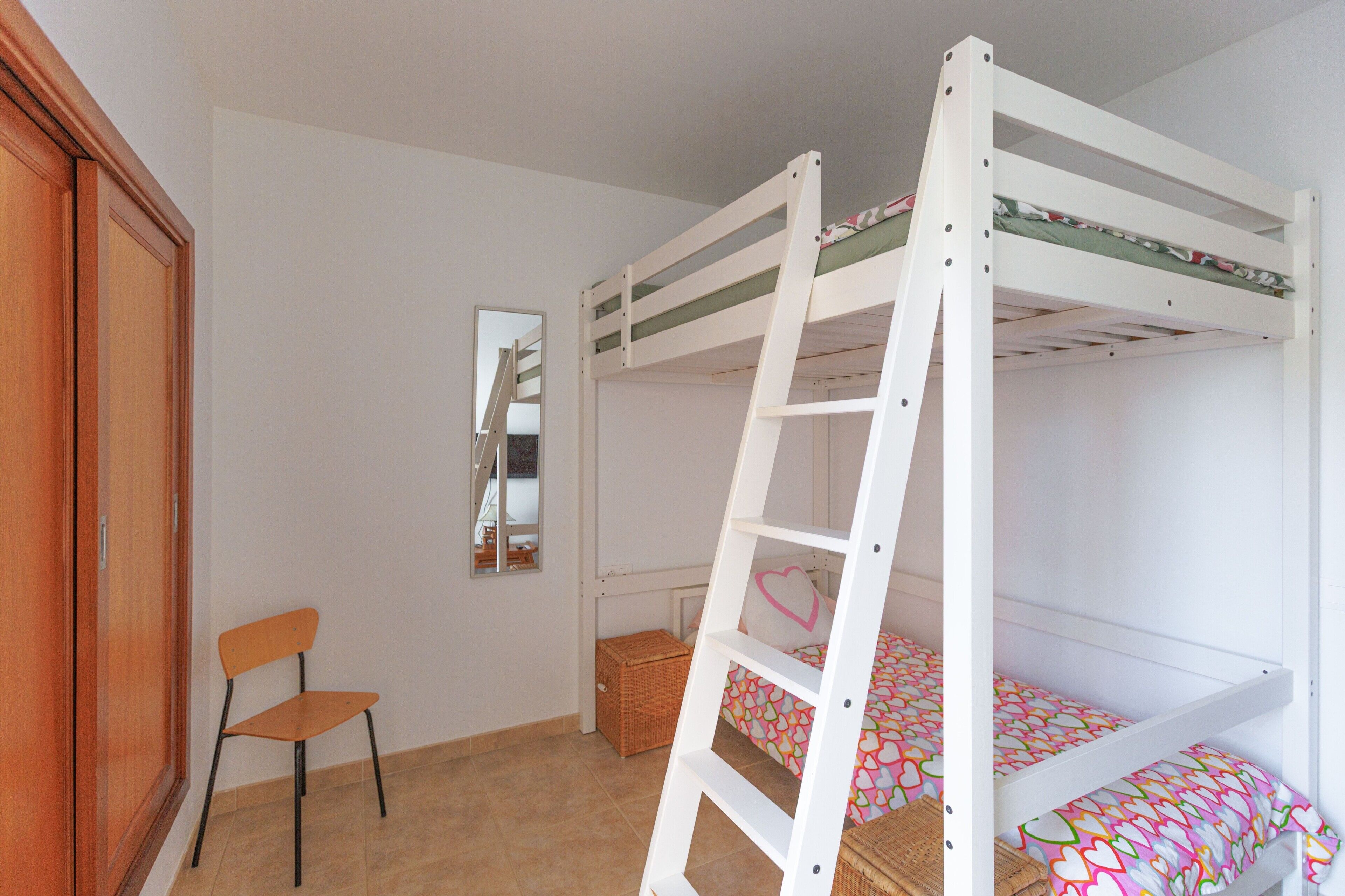 Habitación con literas, una escalera, una silla, un espejo y un armario.